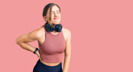 Fototapeta na wymiar Beautiful caucasian young woman wearing gym clothes and using headphones suffering of backache, touching back with hand, muscular pain