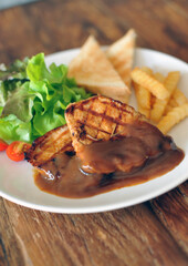plate of grilled pork steak with french fries and salad on wood background