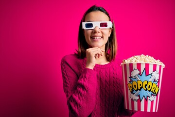Obraz premium Young beautiful girl watching movie using 3d glasses eating box with popcorns with hand on chin thinking about question, pensive expression. Smiling and thoughtful face. Doubt concept.