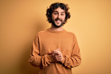 Fototapeta na wymiar Young handsome man with beard wearing casual sweater standing over yellow background with hands together and crossed fingers smiling relaxed and cheerful. Success and optimistic