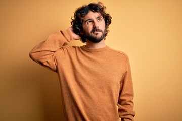 Young handsome man with beard wearing casual sweater standing over yellow background confuse and wondering about question. Uncertain with doubt, thinking with hand on head. Pensive concept.