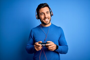 Young handsome gamer man with beard playing video game using joystick and headphones with a happy face standing and smiling with a confident smile showing teeth © Krakenimages.com