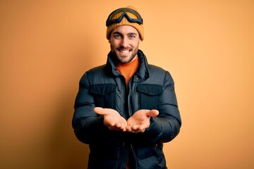 Young handsome skier man with beard wearing snow sportswear and ski goggles Smiling with hands palms together receiving or giving gesture. Hold and protection