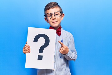 Cute blond kid wearing nerd bow tie and glasses holding question mark smiling happy pointing with hand and finger