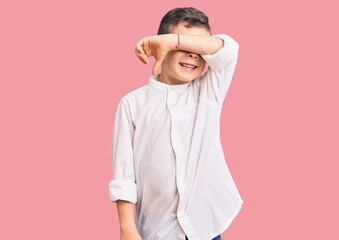 Cute blond kid wearing elegant shirt covering eyes with arm smiling cheerful and funny. blind concept.