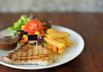 plate of grilled pork steak with french fries and salad on wood background