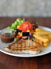 plate of grilled pork steak with french fries and salad on wood background