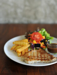 plate of grilled pork steak with french fries and salad on wood background