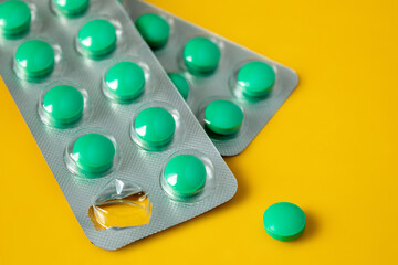 Blisters of green pills and separately one pill on a yellow background. Concept of starting a course of medication and vitamins