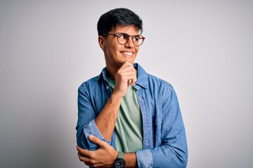 Young handsome man wearing casual shirt and glasses over isolated white background with hand on chin thinking about question, pensive expression. Smiling with thoughtful face. Doubt concept.