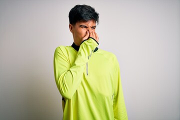Young handsome sportsman doing sport wearing sportswear over isolated white background smelling something stinky and disgusting, intolerable smell, holding breath with fingers on nose. Bad smell