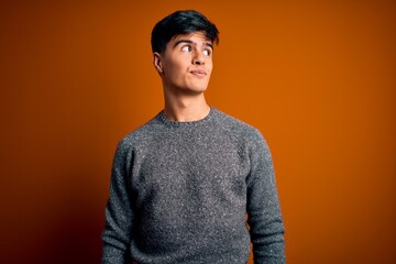 Young handsome man wearing casual sweater standing over isolated orange background smiling looking to the side and staring away thinking.