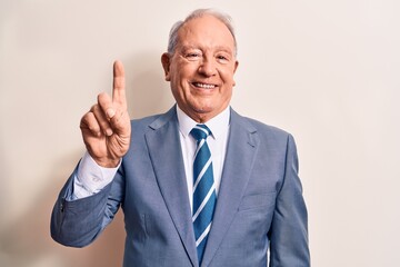 Senior handsome grey-haired businessman wearing elegant suit over white background smiling with an idea or question pointing finger up with happy face, number one