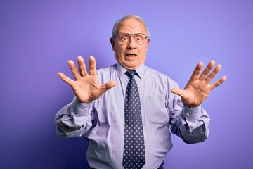 Grey haired senior business man wearing glasses standing over purple isolated background afraid and terrified with fear expression stop gesture with hands, shouting in shock. Panic concept.