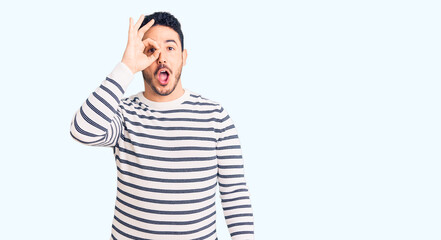 Fototapeta premium Young hispanic man wearing casual clothes doing ok gesture shocked with surprised face, eye looking through fingers. unbelieving expression.