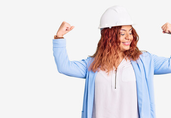 Young latin woman wearing architect hardhat showing arms muscles smiling proud. fitness concept.