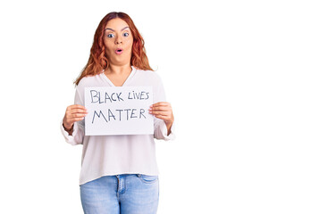 Young latin woman holding black lives matter banner scared and amazed with open mouth for surprise,...