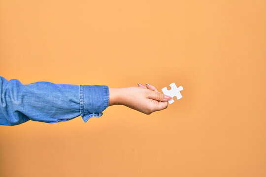 Hand of caucasian young woman holding piece of puzzle over isolated yellow background