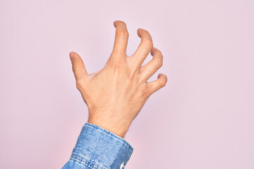 Hand of caucasian young man showing fingers over isolated pink background grasping aggressive and scary with fingers, violence and frustration