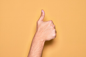 Hand of caucasian young man showing fingers over isolated yellow background doing successful approval gesture with thumbs up, validation and positive symbol