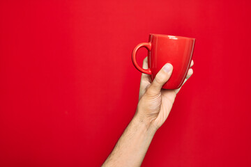 Beautiful hand of man holding cup of coffee over isolated red background