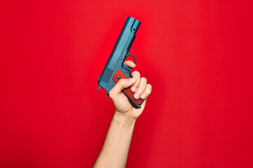 Beautiful hand of man holding gun over isolated red background