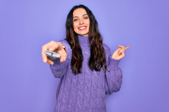 Young beautiful woman using television remote control over isolated purple background very happy pointing with hand and finger to the side