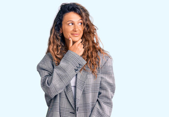 Young hispanic woman with tattoo wearing business oversize jacket with hand on chin thinking about question, pensive expression. smiling with thoughtful face. doubt concept.