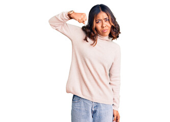 Young beautiful mixed race woman wearing winter turtleneck sweater strong person showing arm muscle, confident and proud of power