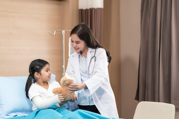 Young smiling female pediatrician doctor and child patient with teddy bear in the health medical center, talking positively with kid for the encouragement