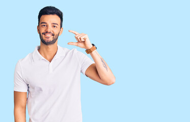 Young handsome hispanic man wearing casual clothes smiling and confident gesturing with hand doing small size sign with fingers looking and the camera. measure concept.