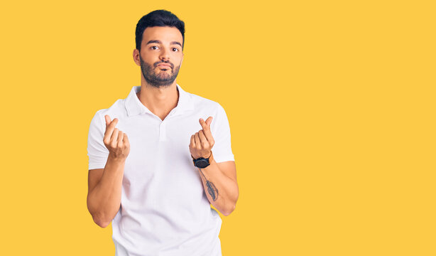 Young handsome hispanic man wearing casual clothes doing money gesture with hands, asking for salary payment, millionaire business