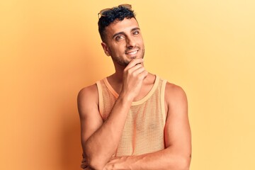 Young hispanic man wearing casual clothes smiling looking confident at the camera with crossed arms and hand on chin. thinking positive.