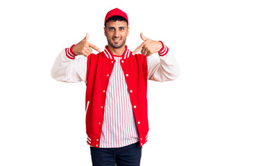 Young hispanic man wearing baseball uniform looking confident with smile on face, pointing oneself with fingers proud and happy.