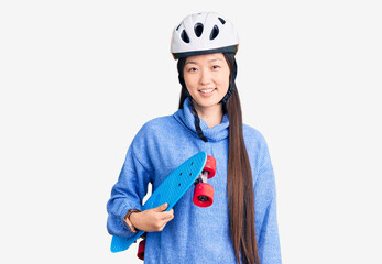 Young beautiful chinese woman wearing security helmet holding skate looking positive and happy standing and smiling with a confident smile showing teeth