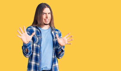 Young adult man with long hair wearing casual shirt disgusted expression, displeased and fearful...