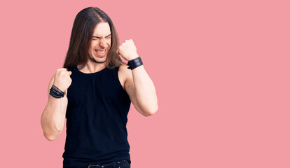 Obraz premium Young adult man with long hair wearing goth style with black clothes celebrating surprised and amazed for success with arms raised and eyes closed. winner concept.