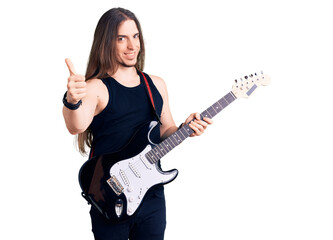 Fototapeta premium Young adult man with long hair playing electric guitar smiling happy and positive, thumb up doing excellent and approval sign