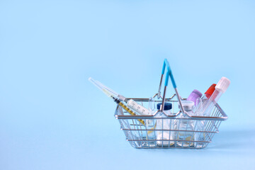 Shopping basket with syringes, injections, vaccines and blood tubes on a blue background. Covid 19 vaccination