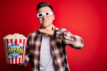 Young handsome caucasian man wearing 3d movie glasses and eating popcorn cutting throat with hand as knife, threaten aggression with furious violence