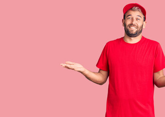 Naklejka premium Young handsome blond man wearing t-shirt and cap clueless and confused expression with arms and hands raised. doubt concept.