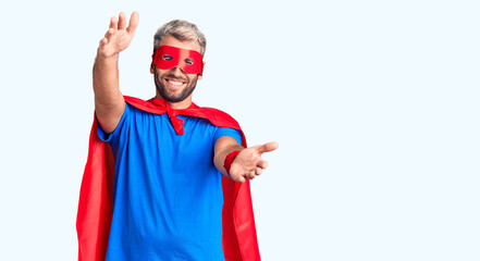 Young blond man wearing super hero custome looking at the camera smiling with open arms for hug. cheerful expression embracing happiness.