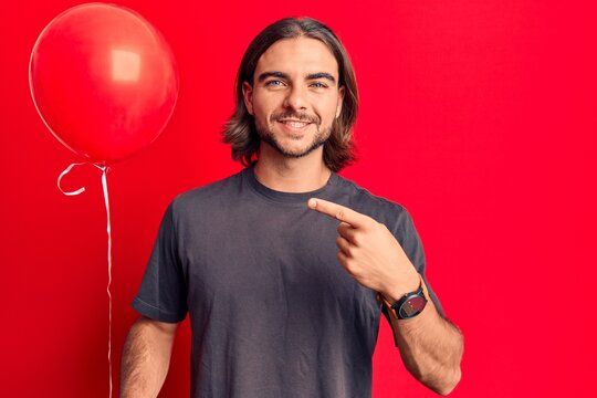 Young handsome man holding balloon smiling happy pointing with hand and finger