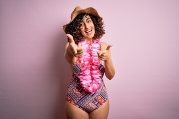 Young beautiful arab woman on vacation wearing swimsuit and hawaiian lei flowers pointing fingers to camera with happy and funny face. Good energy and vibes.