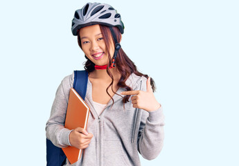 Young beautiful chinese girl wearing student backpack and bike helmet holding book pointing finger to one self smiling happy and proud