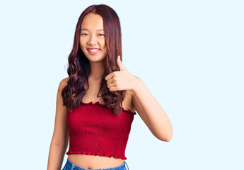 Young beautiful chinese girl wearing casual clothes doing happy thumbs up gesture with hand. approving expression looking at the camera showing success.