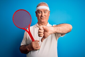 Middle age hoary sportsman playing tennis using racket over isolated blue background with angry face, negative sign showing dislike with thumbs down, rejection concept