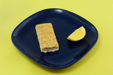 Lemon rind oat bar with icing and lemon wedge on blue snack plate