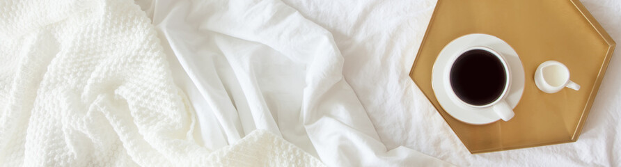 Cozy breakfast in bed, cup of coffee and milk on the grey fabric, space for text. Alarm clock for seven in the morning.