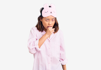 Young beautiful chinese girl wearing sleep mask and pajama feeling unwell and coughing as symptom for cold or bronchitis. health care concept.